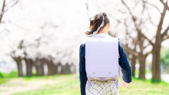 桜並木を歩く小学生の後ろ姿。ランドセルを背負って登校する女の子