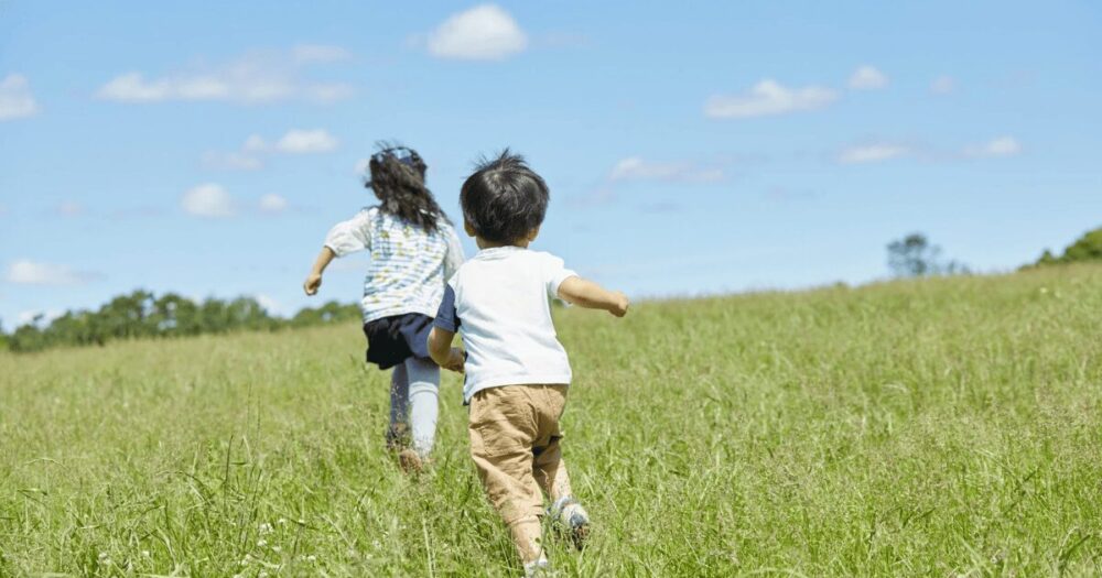 夏の草原を走る子どもたちの後ろ姿の写真。自由な行動が増える夏休みのイメージにぴったり